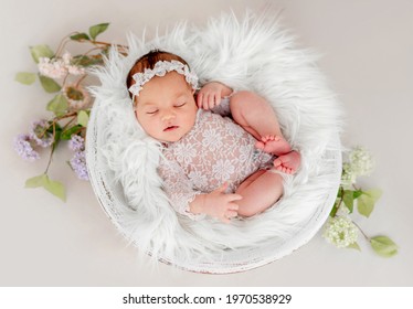 Beautiful newborn baby girl wearing lace costume ana wreath sleeping in basin filled white fur during studio photoshoot. Cute portrait of infant child napping