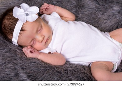 Beautiful newborn baby girl wearing a headband asleep on faux fur