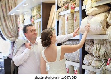 Beautiful Newly Married Couple Choose Bedding In Store, Looks At The Blanket