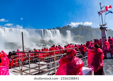 Beautiful Niagara Falls, on the famous Falls boat tour, the Canadian and American flag flying on the mast of Niagara Cruise Boat with tourist wearing rain jackets.