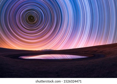 Beautiful night landscape, old volcano, crater lake. The colorful star trails on the sky. Night timelapse photography.