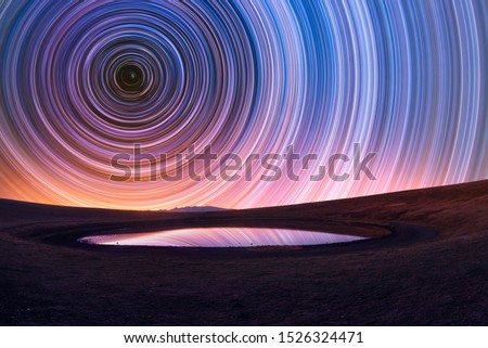 Beautiful night landscape, old volcano, crater lake. The colorful star trails on the sky. Night timelapse photography.