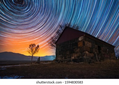 Beautiful Night Landscape, Small Church And Star Trails. The Colorful Star Trails On The Sky With Orientation On The North Star. Night Time Lapse Photography.