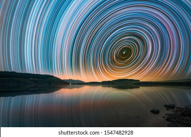 Beautiful Night Landscape With Small Lake And Mountains. The Colorful Star Trails On The Sky. Night Time Lapse Photography.