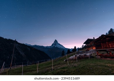 Beautiful night scene of Matterhorn iconic mountain with starry and flock of Valais blacknose sheep by the wooden hut on hill in the night at Zermatt, Switzerland - Shutterstock ID 2394511689