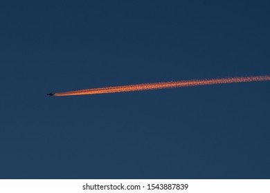 A Beautiful Night Scene Of A Plane Flying High In The Sky And Leaving A Long Orange Trail Behind It