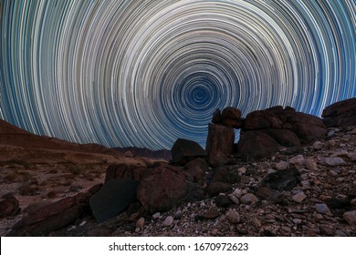 A beautiful night sky landscape with circular star trails, and interesting rock formations in the foreground and mountains on the horizon, in the Richtersveld National Park, South Africa.