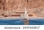 Beautiful Nile scenery with traditional Felluca sailing boat in the Nile Hatshepsut Temple at sunrise in Valley of the Kings and red cliffs western bank of Nile river - Luxor- Egypt