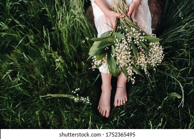 A beautiful nine-year-old blonde in a long white dress, holding a bouquet of lilies of the valley,close-up of a girl holding flowers of the valley.Summer, sunset. - Powered by Shutterstock