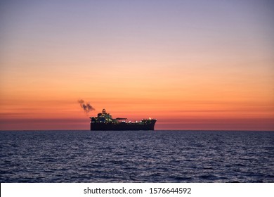 Beautiful  ocean sunset, with colorful clouds, dark waves and silhouette of ship, oil tanker on the horizon with smoke coming from the ships exhaust pipe. - Powered by Shutterstock