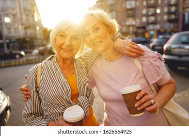 Beautiful Old Friends Hugging And Holding Their Coffee Cups In The Street