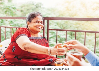 Beautiful old Indian woman offering laddu (traditional sweets) to the guest on the balcony - Powered by Shutterstock