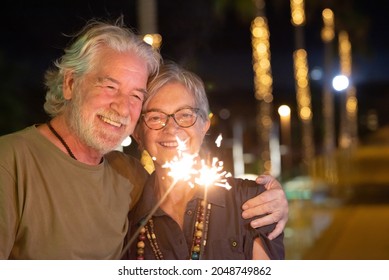 Beautiful old senior couple in outdoor at night having fun with sparkles lights. Two smiling retired people hugging with love