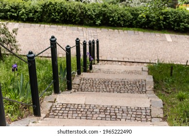 Beautiful old staircase. A stone staircase with colorful stones descends to the path. A small black railing and railing. - Shutterstock ID 1965222490