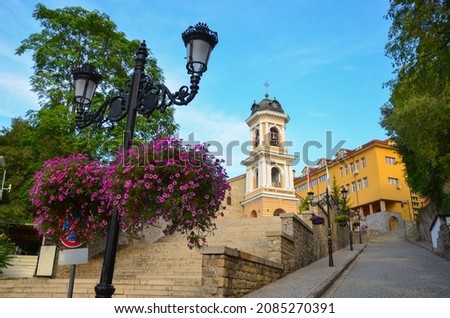 Beautiful old town with the Holy Mother of God Church in Plovdiv, Bulgaria. Purple blooming flowers, cobbled street and traditional houses. Blue sky above.