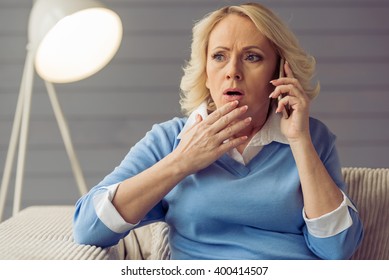 Beautiful old woman in casual clothes is talking on the mobile phone and showing surprise while sitting at home