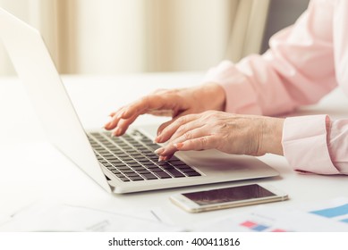 Beautiful old woman in classic shirt is using a laptop while working at home, close-up - Powered by Shutterstock