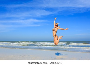 Beautiful Older Late 40s Woman With Nice Healthy Body In Bikini Jumping On Beach At Seaside With Blue Sky, Freedom Concept And Copy Space, Happy Lifestyle