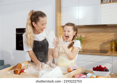 Beautiful Older Sister With Younger One Having Fun In Moder Light Kitchen Cooking Baking Cake Cookies Biscuits. Kneading Dough. Younger Girl Clapping In Hands With Flour.