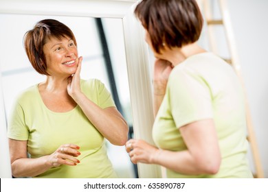 Beautiful Older Woman Looking At Her Face With A Smile Into The Mirror