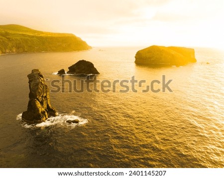 Beautiful orange sunset behind the rock cliffs in ocean water on Sao Miguel Island, Portugal - aerial drone view.