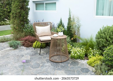 Beautiful outdoor house patio with stone carpet flooring, growing green flowers and plants, and table with chairs. 