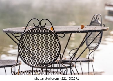 Beautiful Outdoor Iron Dining Set By A Peaceful Lake. Concept Of A Relaxing Breakfast On Vacation. Shallow Focus For Effect On The Top Of The Chair.