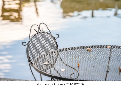 Beautiful Outdoor Iron Dining Set By A Peaceful Lake. Concept Of A Relaxing Breakfast On Vacation. Shallow Focus For Effect On The Top Of The Chair.