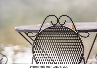 Beautiful Outdoor Iron Dining Set By A Peaceful Lake. Concept Of A Relaxing Breakfast On Vacation. Shallow Focus For Effect On The Top Of The Chair.