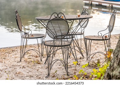 Beautiful Outdoor Iron Dining Set By A Peaceful Lake. Concept Of A Relaxing Breakfast On Vacation. Shallow Focus For Effect On The Top Of The Chair.