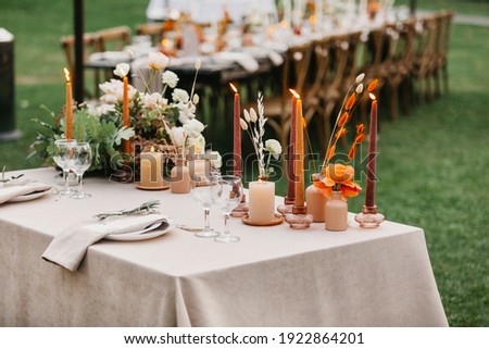Beautiful outdoor wedding decoration in city. Candles, dried flowers and accessories, bouquets and glasses on table with linen tablecloth on newlywed table on green lawn, flat lay, free space, nobody