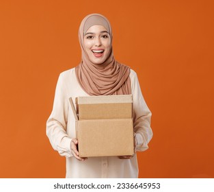 Beautiful overjoyed young smiling muslim woman in traditional religious hijab holding an open cardboard box isolated on orange studio background
 - Powered by Shutterstock