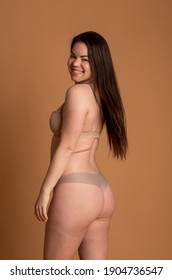 Beautiful overweight woman in beige swimsuit on pink background