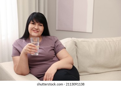 Beautiful Overweight Woman With Glass Of Water On Sofa At Home