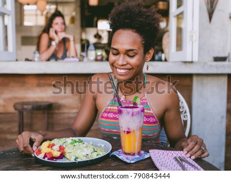 Beautiful pacific islander girl in vegetarian cafe for breakfast with wrap and salad on the plate and smoothie in glass