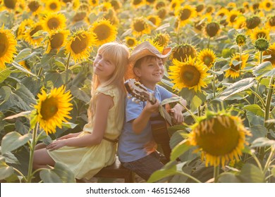 Beautiful pair of small farmers. Boy and girl in a field of sunflowers, the boy playing the guitar