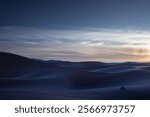 Beautiful panorama of the dusk in the Sahara desert in Morocco. The sun has set and the dunes form soft contrasts of light and shadow. The image inspires the cold of the desert night