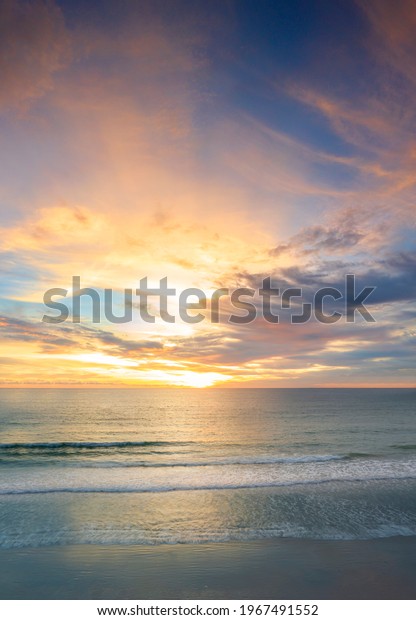 Beautiful of panorama vertical sunset over the clam sea\
with cloud sky background. Sunset over tropical beach. Nature\
summer  concept. Peak sunset over sea with yellow light reflect on\
sea water. 