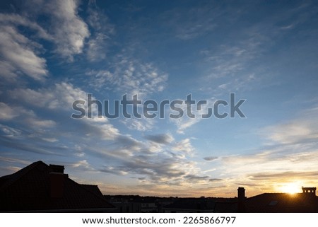 Beautiful panoramic sky with clouds at sunset. Ð¡ontour of roofs of houses. Blue sky, cumulus clouds. Orange sunset.