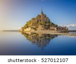 Beautiful panoramic view of famous Le Mont Saint-Michel tidal island with deep blue water and clear reflections in golden evening light at sunset in summer, Normandy, northern France