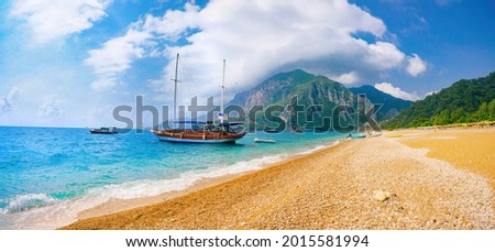 Beautiful panoramic view of sea and beach Cirali, Kemer, Antalya, Turkey. Ship against backdrop of mountains and blue sky with clouds on sunny day.