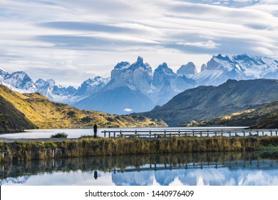 Beautiful panoramic view small people standing at the dock from the lake with Cuernos, horn mountains peak with lenticular cloud in autumn, Torres del Paine national park, south Patagonia, Chile.