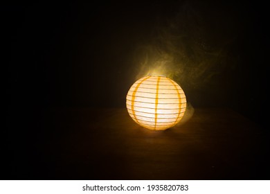 Beautiful paper lantern glowing on wooden table in dark. Selective focus - Powered by Shutterstock