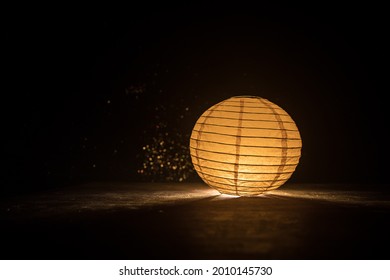 Beautiful paper lantern glowing on wooden table in dark. Selective focus - Powered by Shutterstock