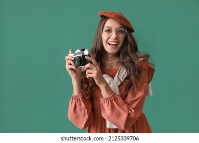 Beautiful Parisian woman holding vintage photo camera on green background