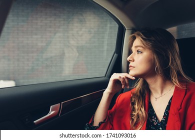 Beautiful passenger on taxi. Moody image. Sad woman thinking while sit on back seat of luxury premium vehicle. Young lady wearing stylish casual red jacket
