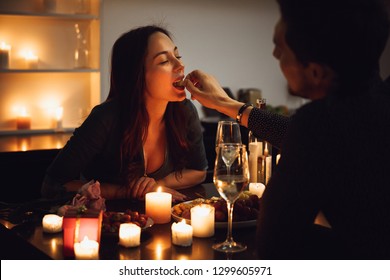 Beautiful Passionate Couple Having A Romantic Candlelight Dinner At Home, Feeding Each Other