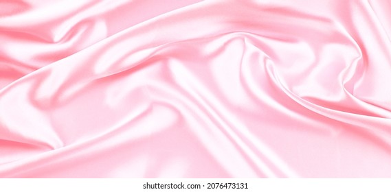 Beautiful pastel pink background with drapery and wavy folds of silk satin material texture. Top view