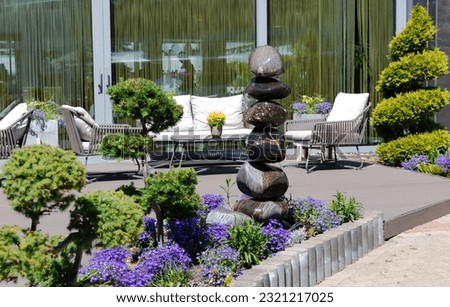 A beautiful patio with a small stone fountain, trimmed thuja and summer wicker furniture. Concept of summer space design. 
