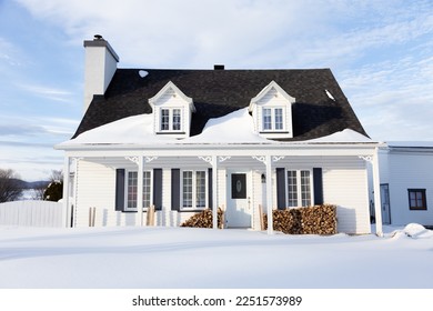 Beautiful patrimonial white French-style clapboard house with dormer windows, black shutters and porch in snowy rural land, Quebec City, Quebec, Canada 